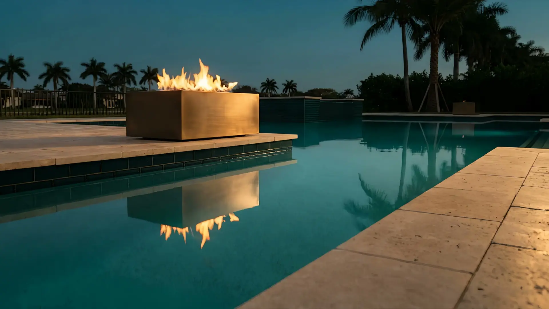 Custom gunite pool with glass-tile spa wall and a bronze fire bowl burning at blue hour in West Palm Beach